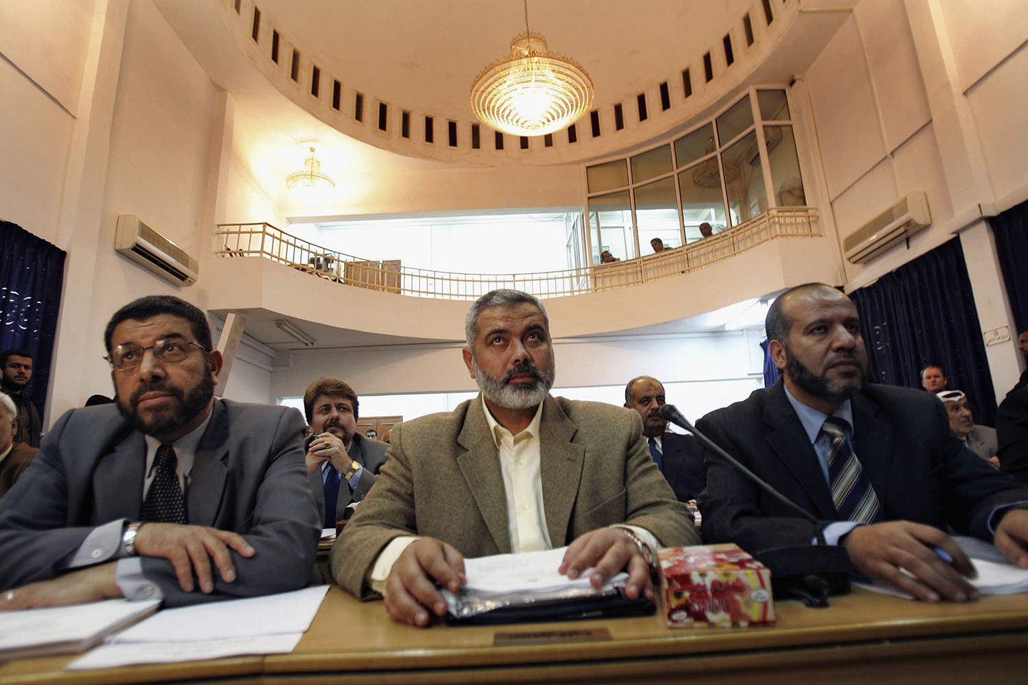رئيس الوزراء المكلف إسماعيل هنية (في الوسط)، يجلس على طاولة مع رجلين آخرين في غرفة رسمية كبيرة أثناء حضورهم الجلسة الأولى للمجلس التشريعي الفلسطيني الذي تقوده حماس في مدينة غزة في عام 2006.